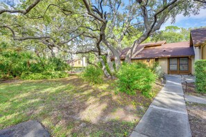 A residential area with a paved walkway, mature trees, and a house with a brown roof and beige siding. - 5 Mi to Anna Maria Island: Apt w/ Pool Access! (Bradenton)