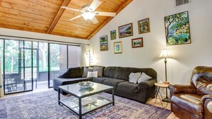 A spacious living room with a glass coffee table, leather sofa, and a leather armchair. There are several framed artworks on the walls and a ceiling fan. - 5 Mi to Anna Maria Island: Apt w/ Pool Access! (Bradenton)