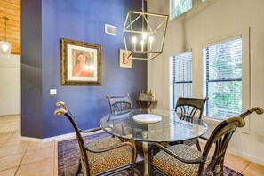 A dining area with a round glass table, four chairs with wooden frames and leopard print cushions, a hanging geometric light fixture, and framed artwork on the wall. - 5 Mi to Anna Maria Island: Apt w/ Pool Access! (Bradenton)