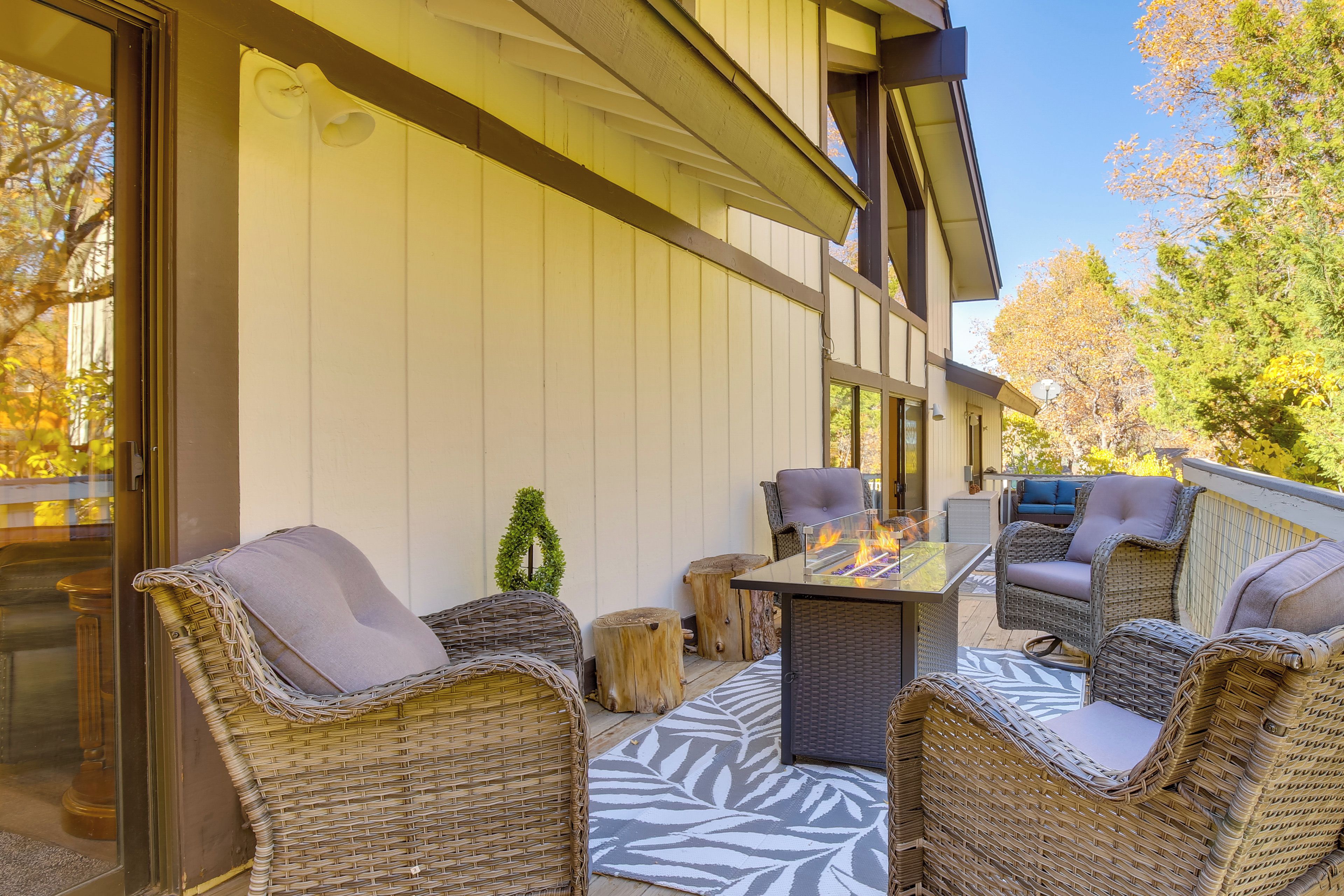 An outdoor patio with wicker furniture, a glass table, and a fire feature.
