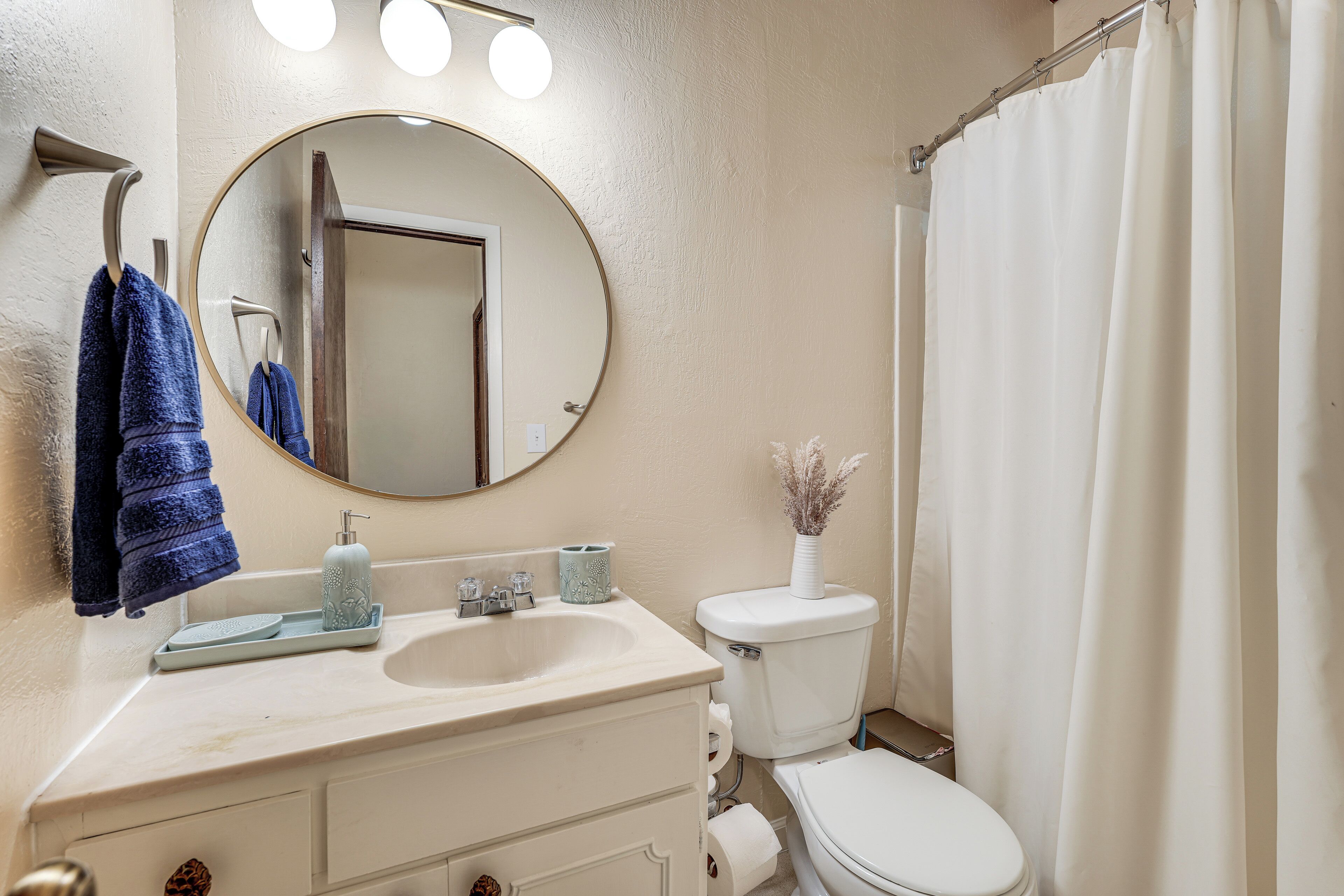 A bathroom with a round mirror, a sink, a toilet, and a shower curtain.