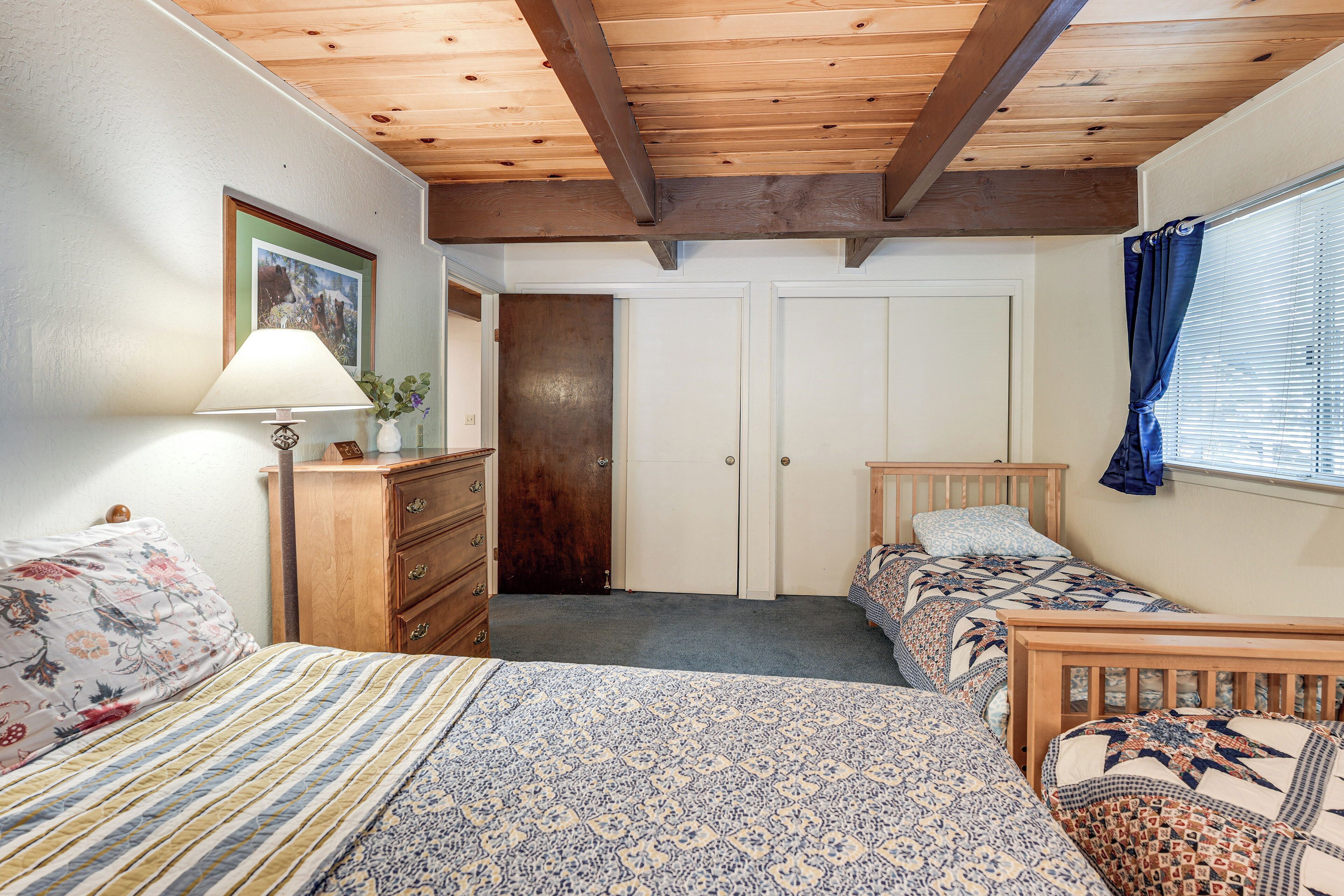 A bedroom with two single beds, a dresser, a lamp, a framed picture, and a door leading to another room.