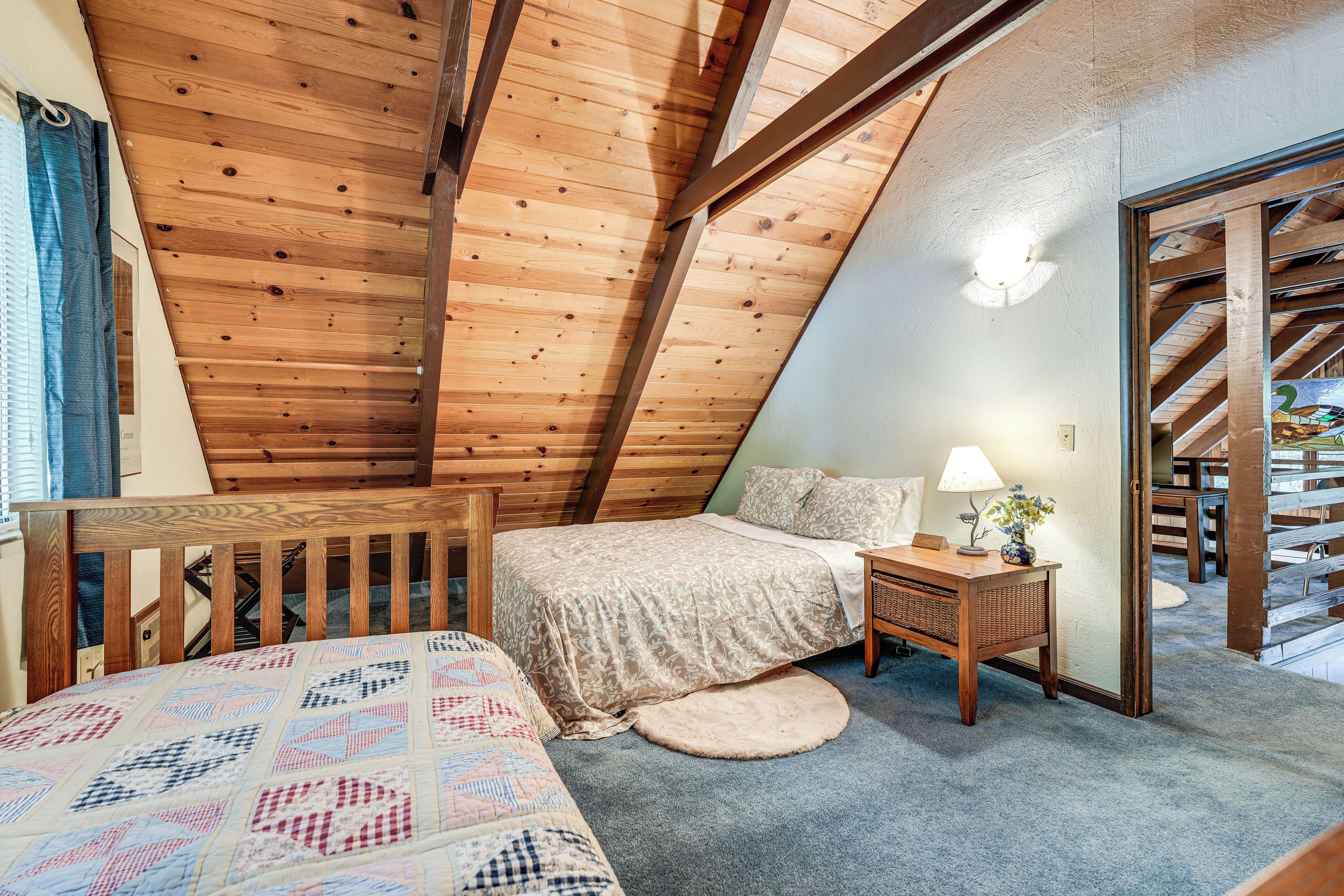 A bedroom with a sloped ceiling, a bed, a nightstand, a lamp, and a small rug.