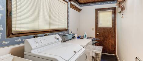 Un cuarto de lavandería con lavadora y secadora, vigas de madera en el techo, y una puerta que da a otra habitación.