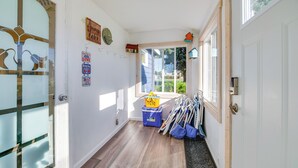 Un pasillo con suelo de madera, una puerta de cristal y una ventana con persianas. Hay varios carteles en la pared y un caja de almacenamiento azul.
