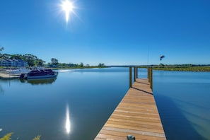 Un muelle de madera que se adentra en aguas tranquilas, con una embarcación amarrada a la izquierda, y un cielo azul despejado.
