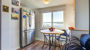 Una cocina con un refrigerador de acero inoxidable, una mesa de comedor con cuatro sillas y un ventanal con vista al agua.