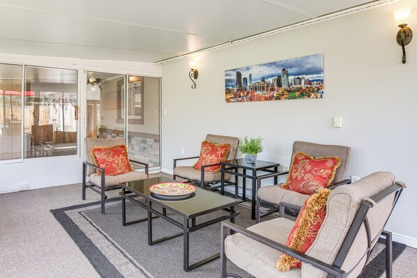 A modern living room with a glass door leading to a patio, a cityscape painting on the wall, and a dining table with a plate.