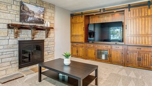 A living room with a stone fireplace, wooden cabinets, a large TV, and a coffee table with a plant. - Suburban Home 9 Mi to Dtwn Denver: Outdoor Oasis! (Aurora)