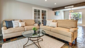 A spacious living room with two beige sofas, a glass coffee table, and a large window providing natural light. - Suburban Home 9 Mi to Dtwn Denver: Outdoor Oasis! (Aurora)