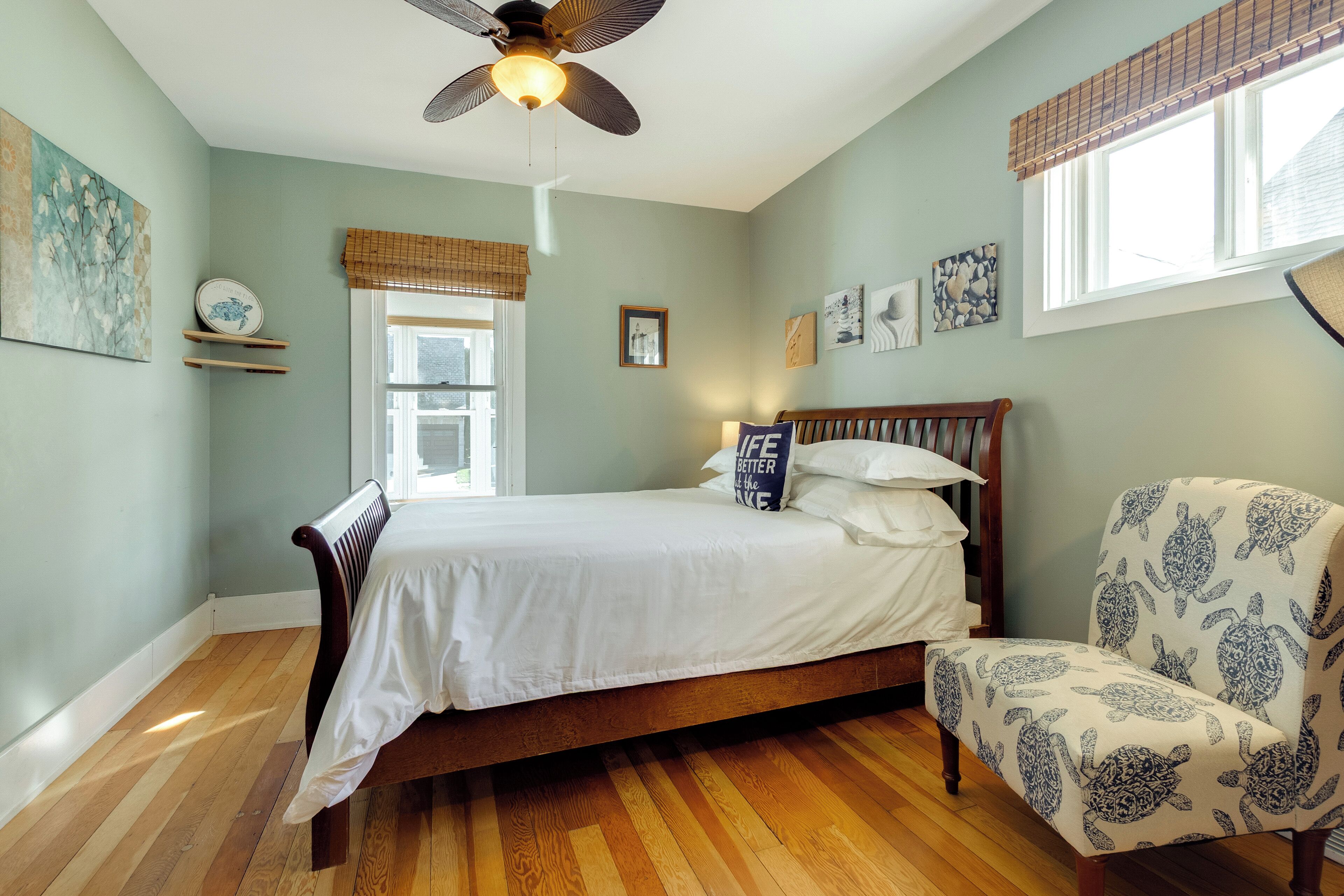 A bedroom with a bed, a chair, a ceiling fan, and artwork on the walls.
