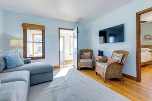 A modern living room with a grey sofa, wicker chairs, a flat-screen TV, and a wooden floor.