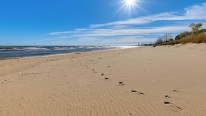 Ein Sandstrand mit Fußabdrücken, die zum Wasser führen, ein klarer Himmel und eine entfernte Küste.