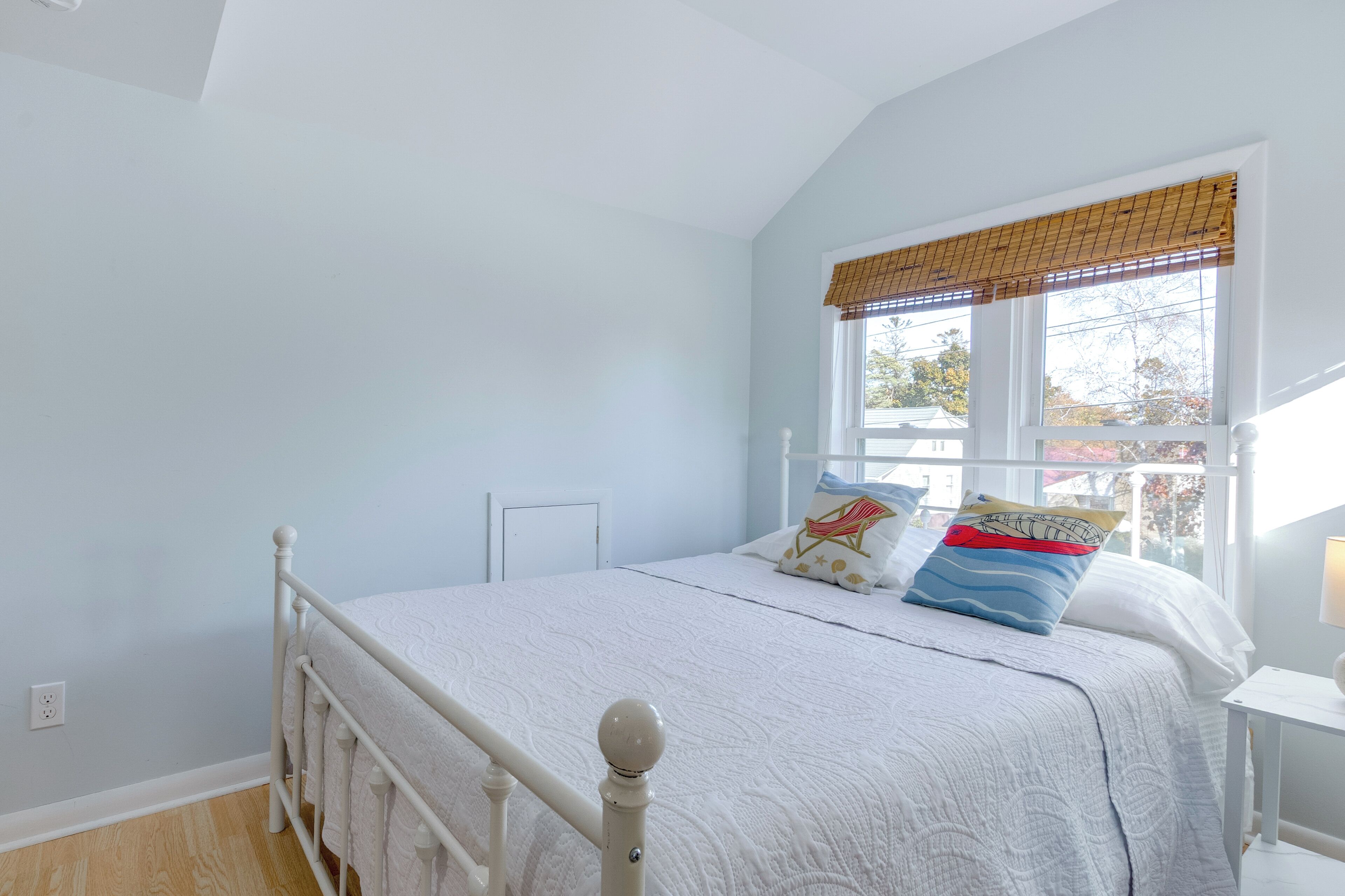 A bedroom with a white bed, a window with blinds, and a white nightstand.