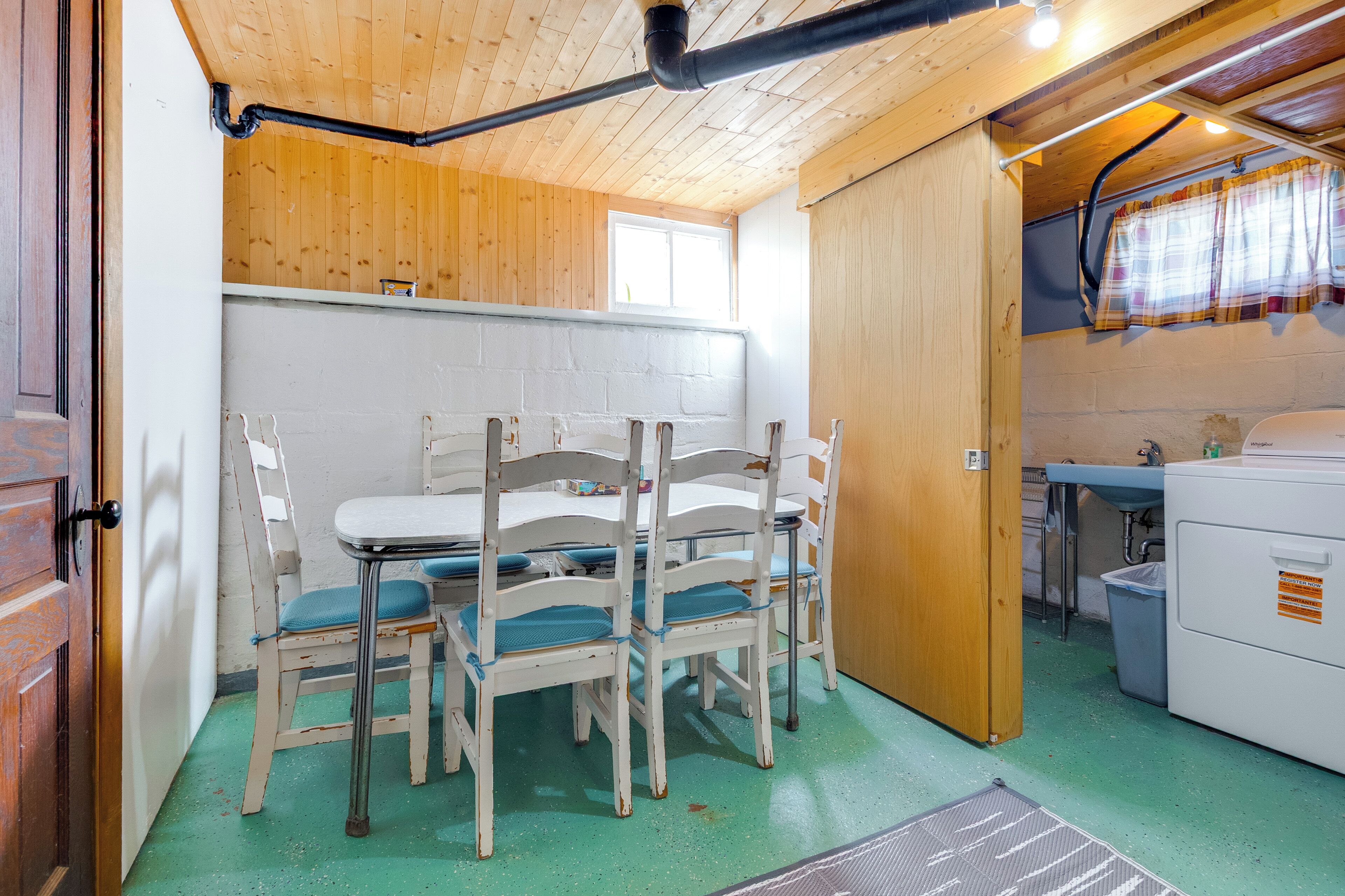 A rustic kitchen with wooden walls, a dining table with chairs, and a window with curtains.