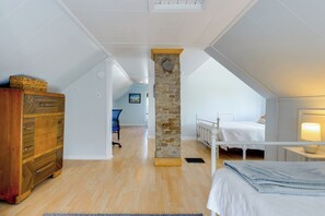 A bedroom with a wooden dresser, a stone pillar, a bed, and a desk with a lamp.
