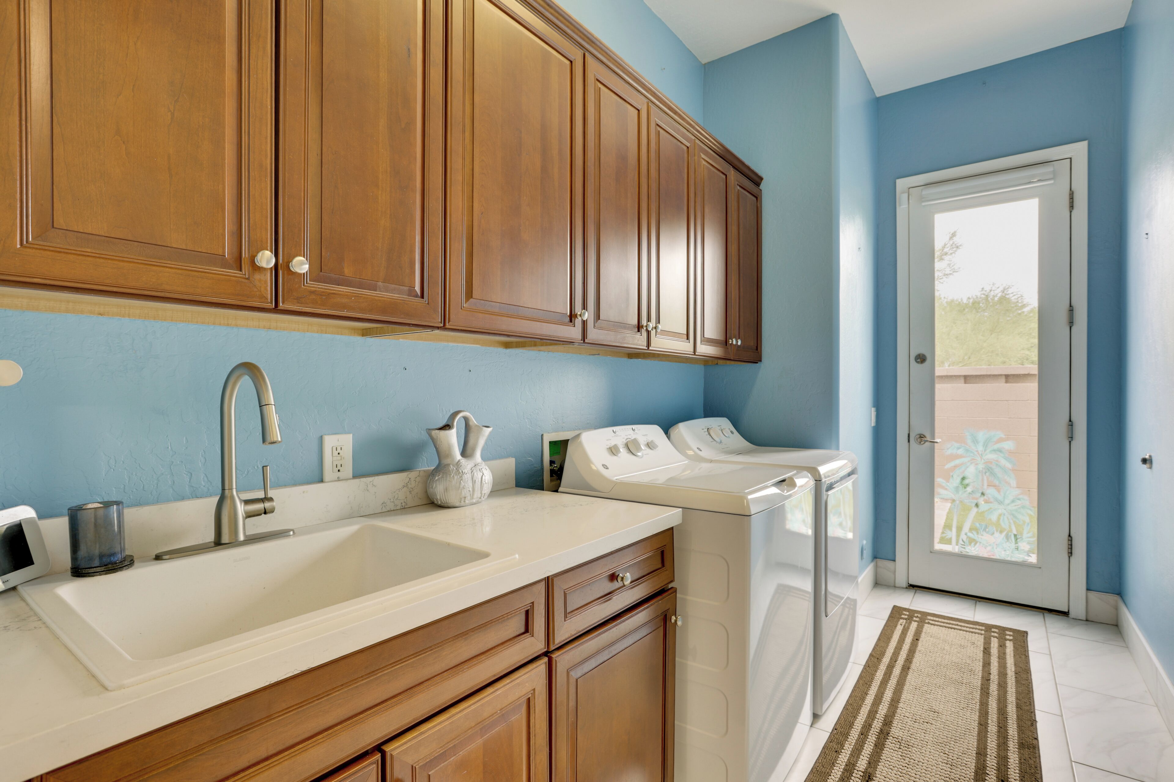 A kitchen with wooden cabinets, a sink, a faucet, a vase, and a washing machine.
