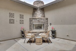 A patio with a stone fireplace, wicker furniture, and potted plants.