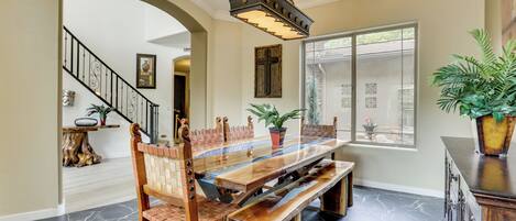 A dining area with a long wooden table, chairs with woven backs, and a chandelier.