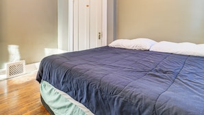 Een slaapkamer met een groot bed, een witte deur en een vloeraansluiting.
