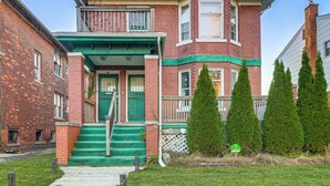 Een twee verdiepingen tellend huis van baksteen met een groene veranda en wenteltrap.