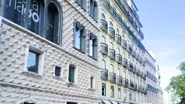 Un edificio storico con una facciata geometrica particolare, numerosi balconi e zone con posti a sedere all'aperto.