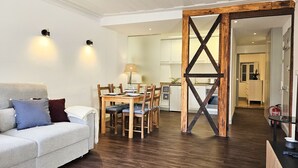 Un soggiorno moderno con divano, tavolo da pranzo e sedie, una cucina sullo sfondo e un pannello in legno.