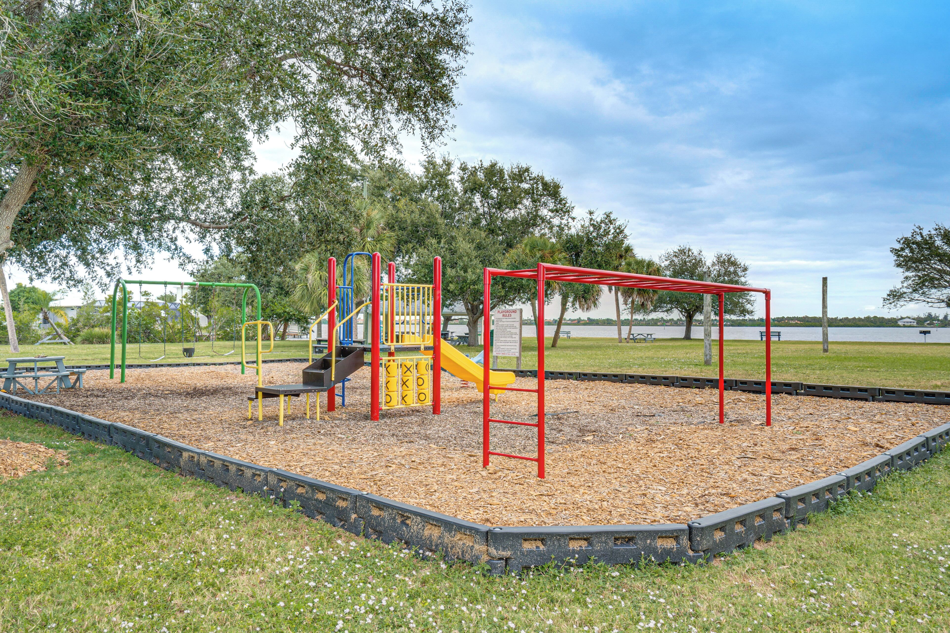 A playground with a slide and swings, surrounded by trees and a lake view.