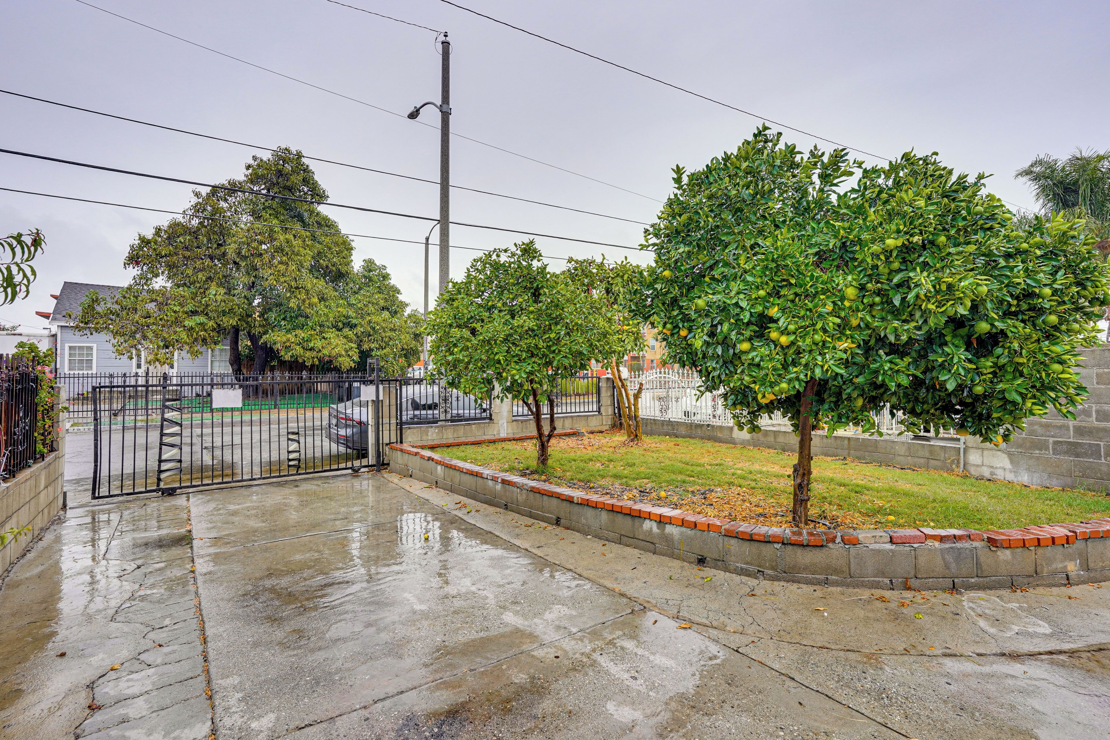 A residential area with a paved sidewalk, a black metal fence, and a tree-lined street.