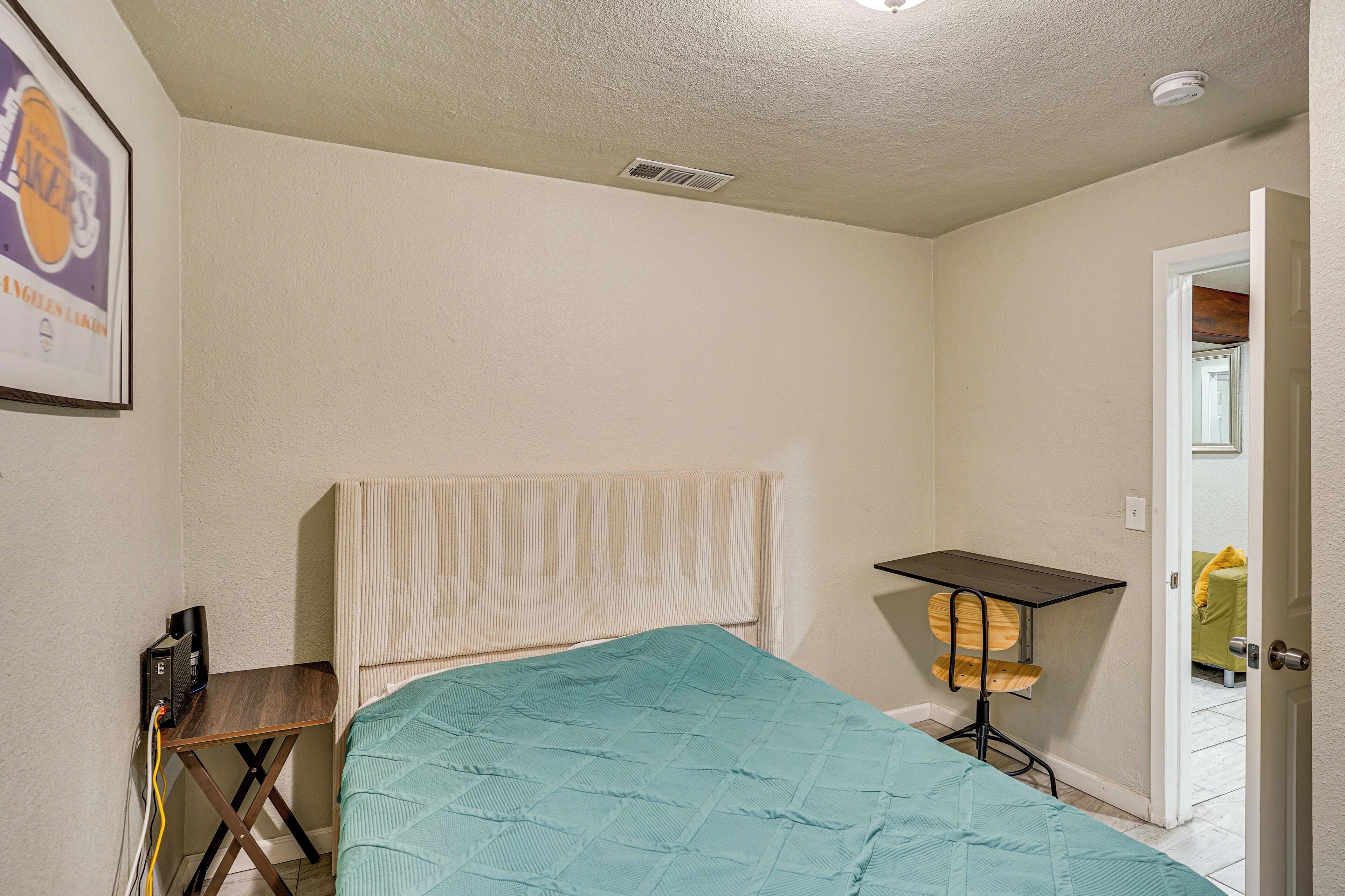 A bedroom with a bed, a desk, a chair, and a framed picture on the wall.