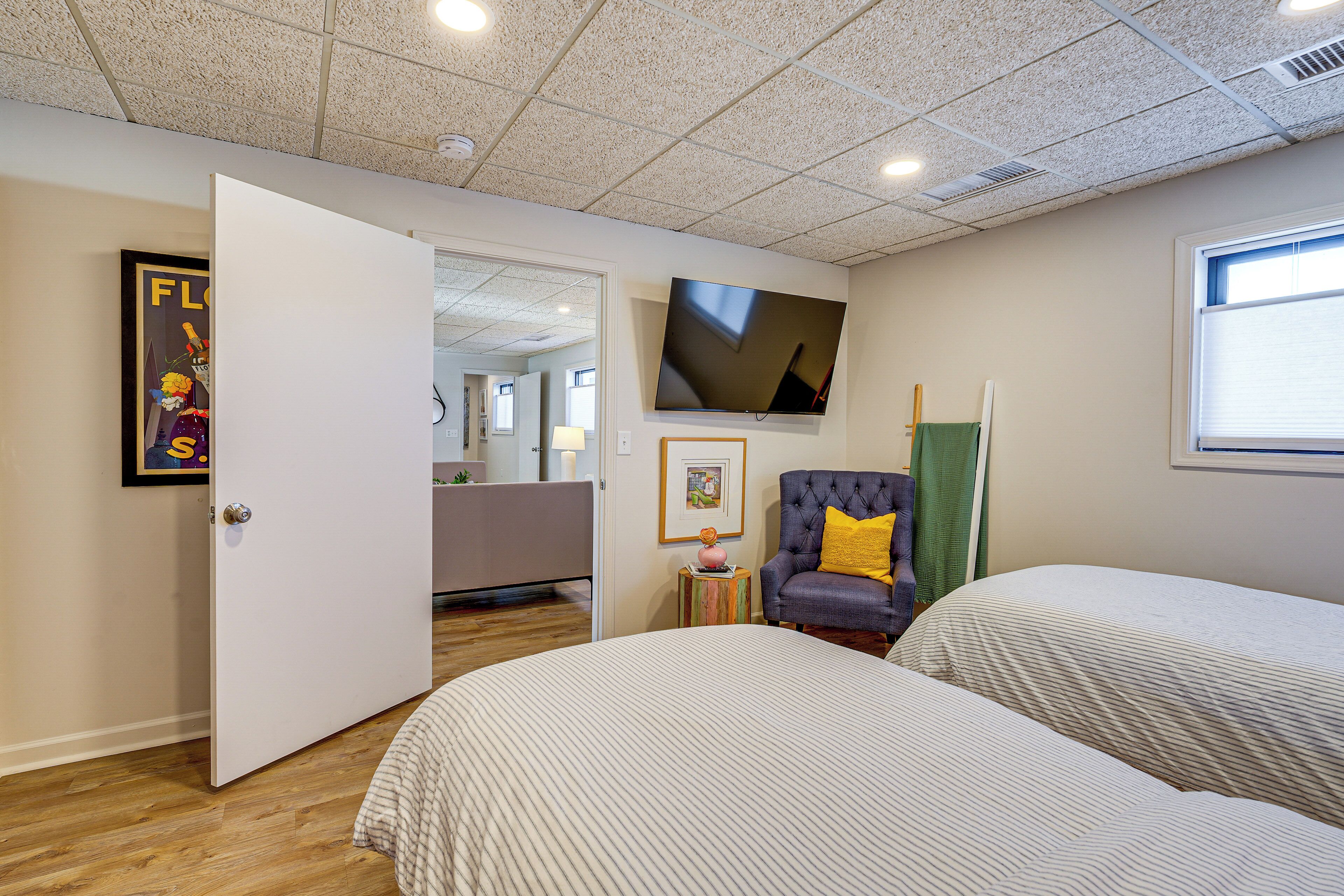 A hotel room with two beds, a television, a chair with a yellow pillow, and a door leading to another room.
