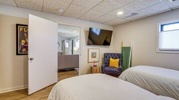 A hotel room with two beds, a television, a chair with a yellow pillow, and a door leading to another room.