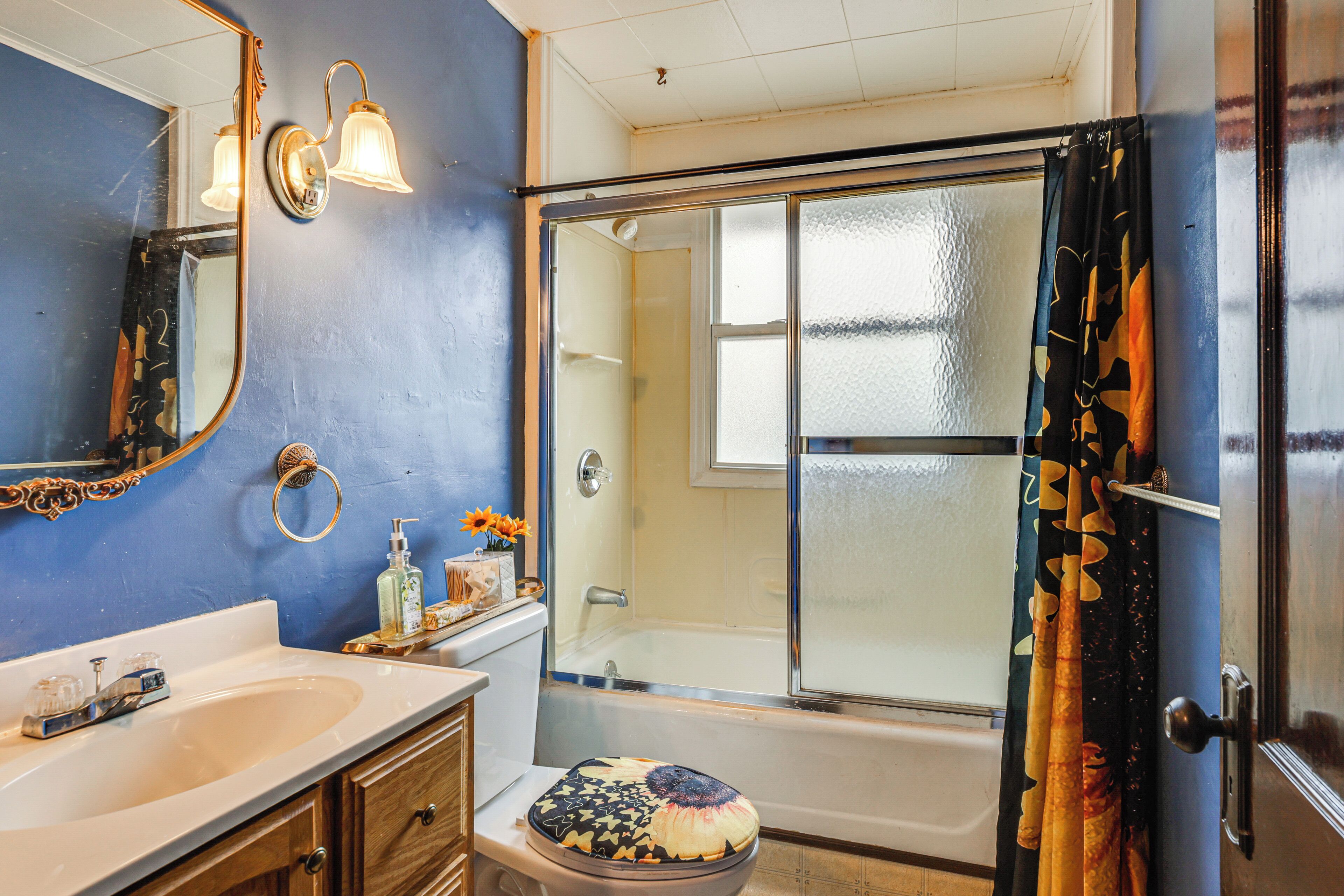 Un baño con bañera, inodoro con tapa decorativa, lavabo y espejo.