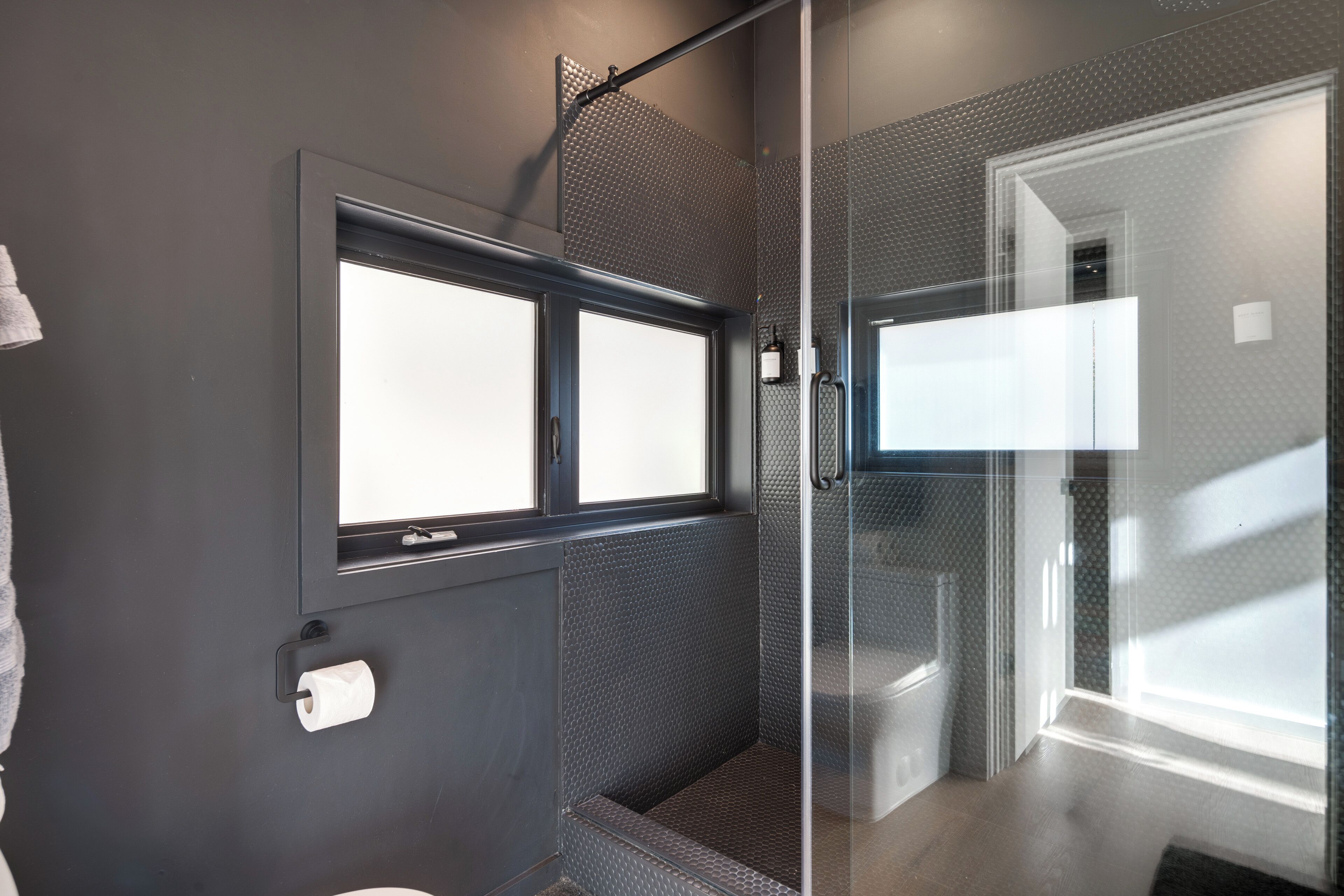 A modern bathroom with a shower area, a toilet, and a window.