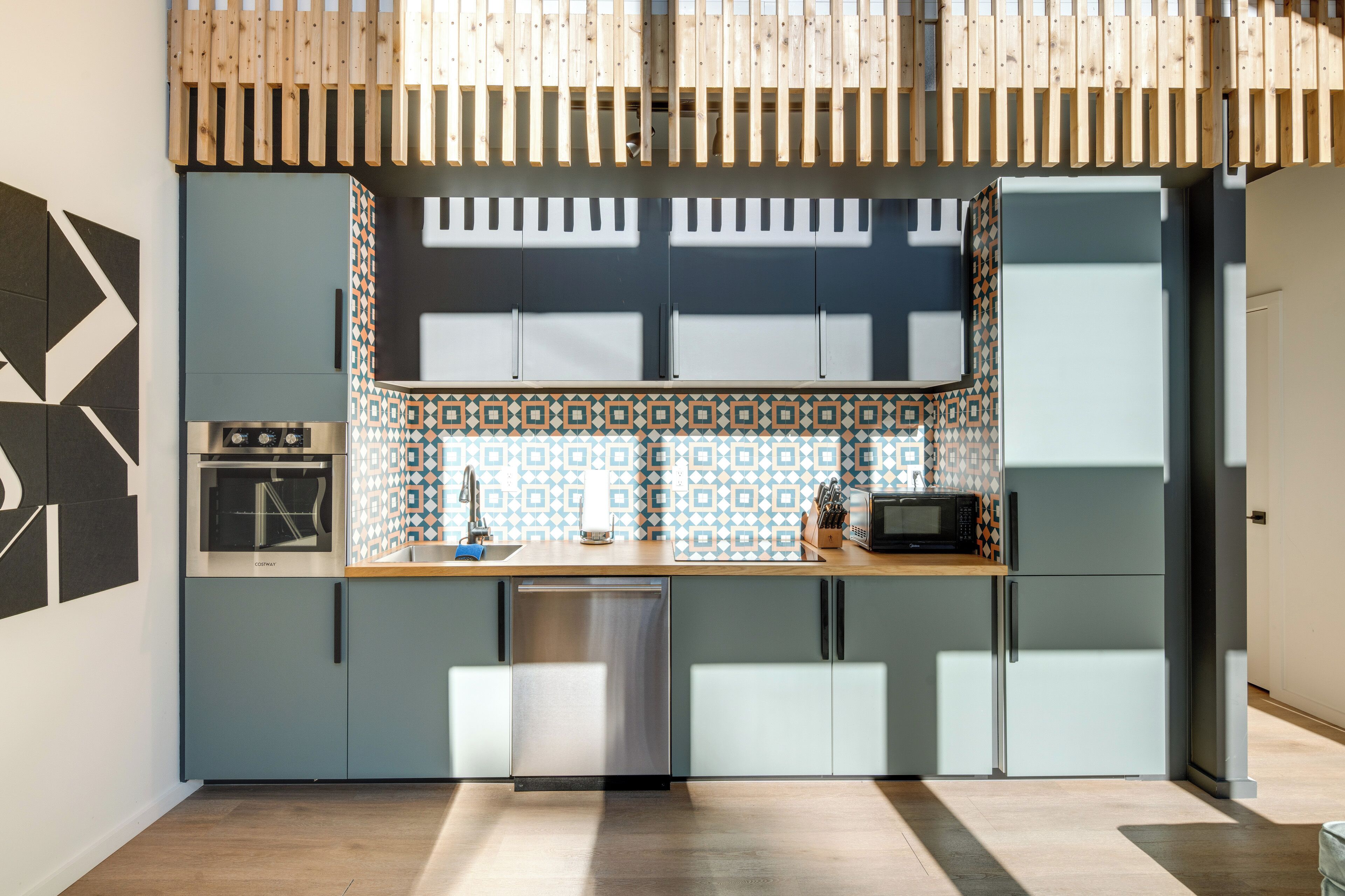 Una cocina moderna con horno empotrado, microondas y lavavajillas, con armarios azul claro y salpicadero decorado.