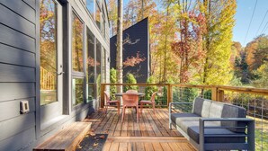 Una terraza de madera con un sofá y sillas, con vistas a un bosque de follaje otoñal.