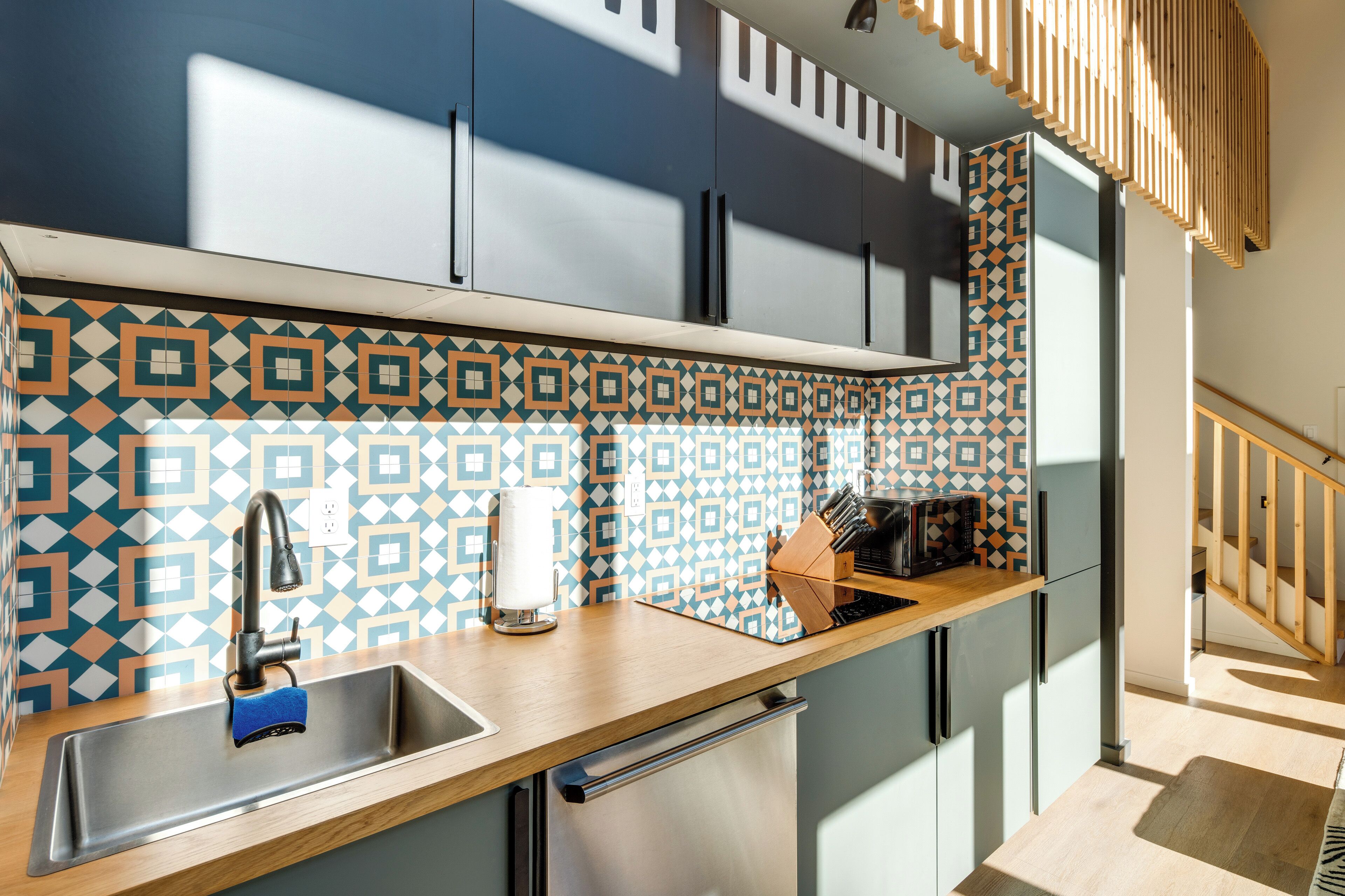 A modern kitchen with a stainless steel sink, wooden countertop, and patterned backsplash.