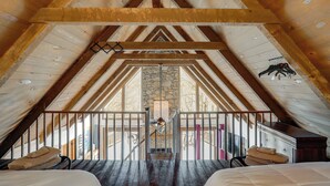 Un dormitorio en ático con techos altos, vigas de madera, una pared de piedra y vistas al exterior.