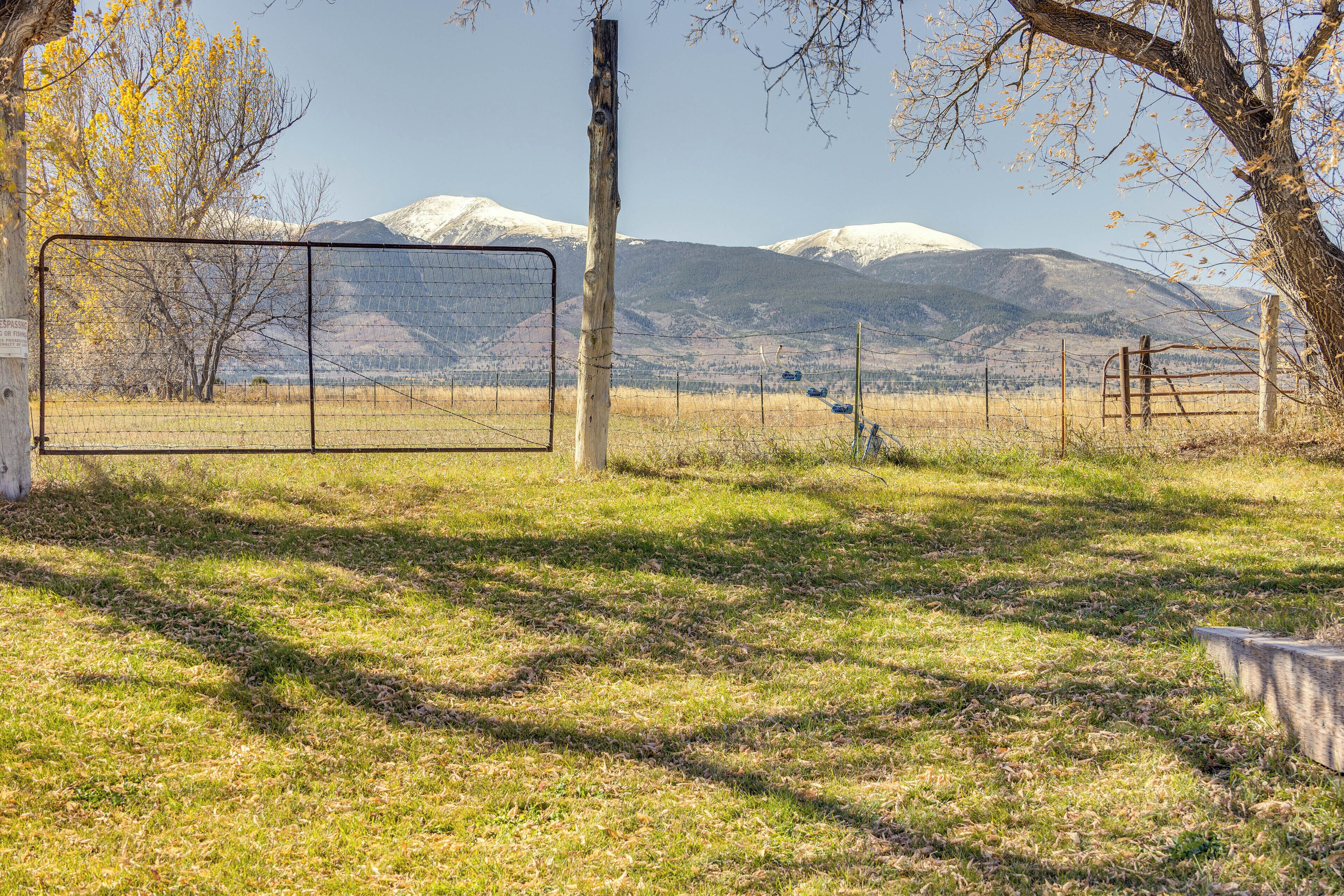 A fenced field with a gate, trees, and mountains in the background.