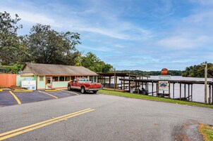 A parking lot with a red truck, a small building with a sign, and a wooden dock extending into a lake.
