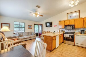 Amplia sala de estar con sofá, mesa de comedor y zona de cocina con armarios de madera y electrodomésticos.