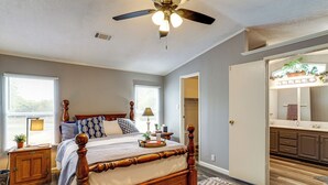 Egy hálószoba, amelyben van egy faágy, egy mennyezeti ventilátor, egy éjjeliszemélyzet, valamint egy fürdőszoba mosdóval és tükörrel.