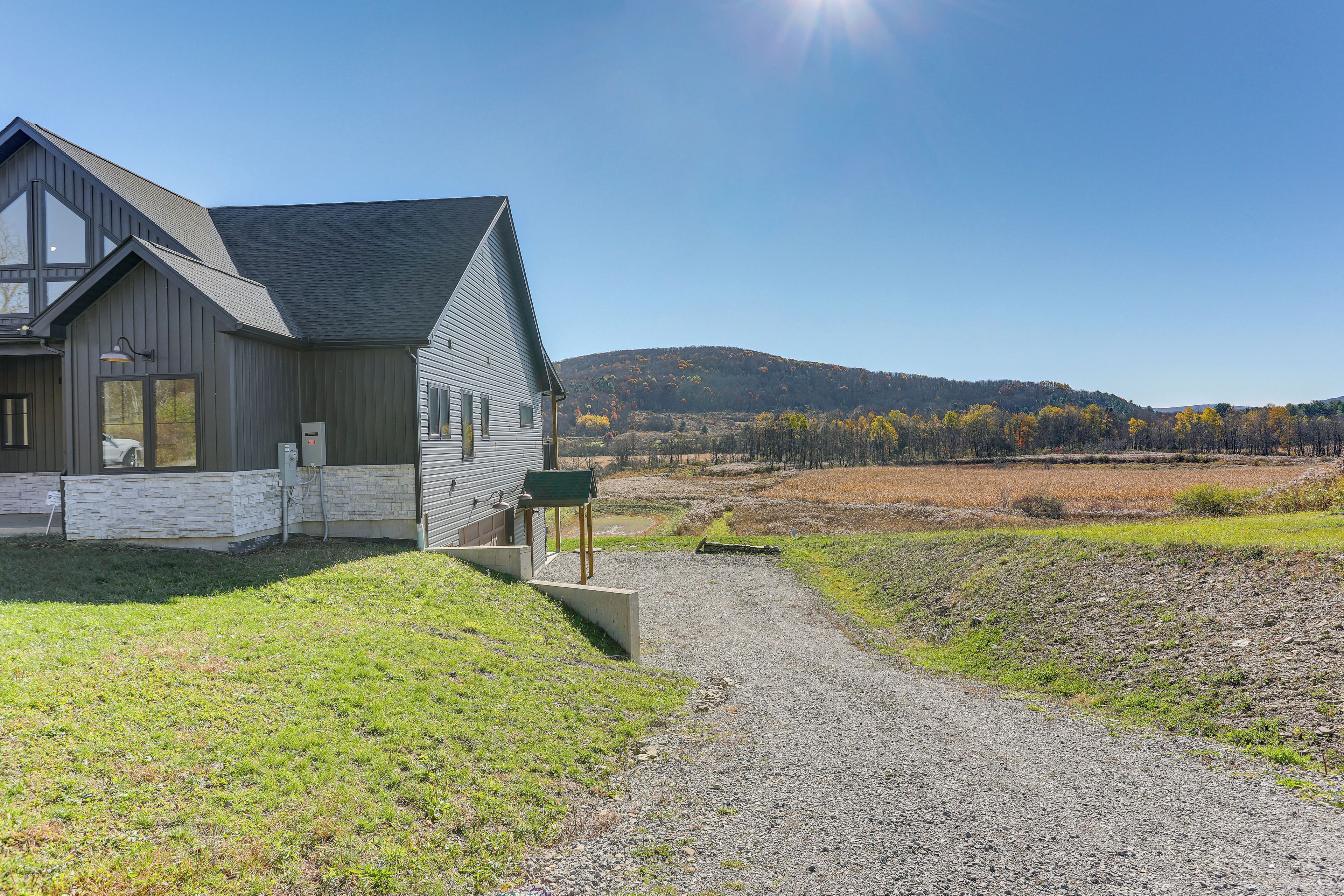 A modern house with a gravel driveway and a view of a hilly landscape.