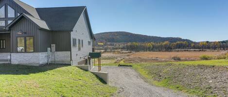A modern house with a gravel driveway and a view of a hilly landscape.