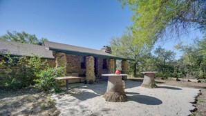 A stone building with a sloped roof, outdoor seating, and two stone tables.