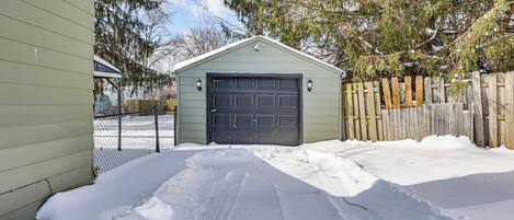 A garage with a dark door, a wooden fence, and snow on the ground.