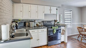 Una cocina con armarios blancos, un lavamanos de acero inoxidable, un microondas, un tostador y un horno.