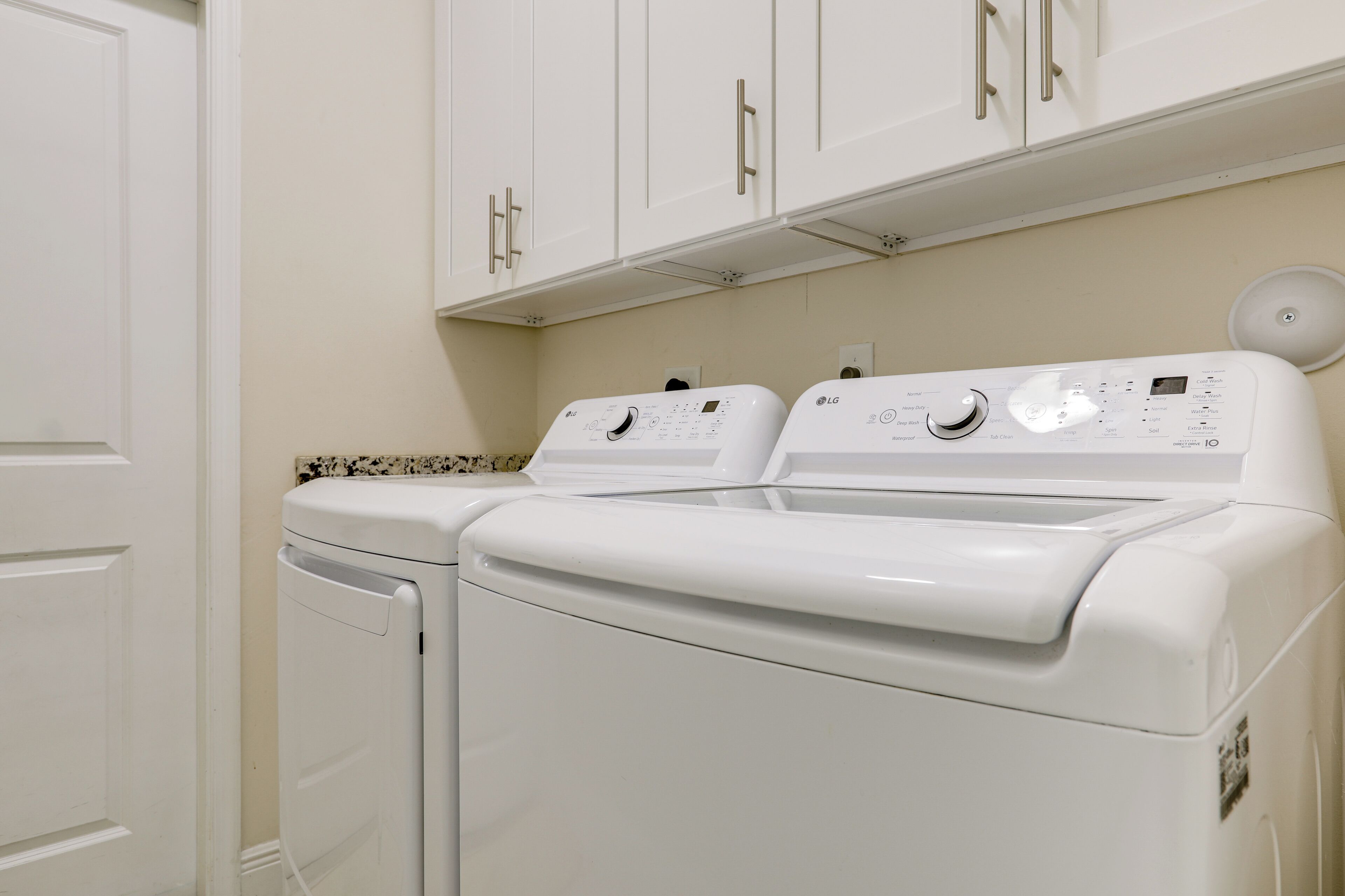 A laundry room with two white front-loading washing machines and cabinets above.