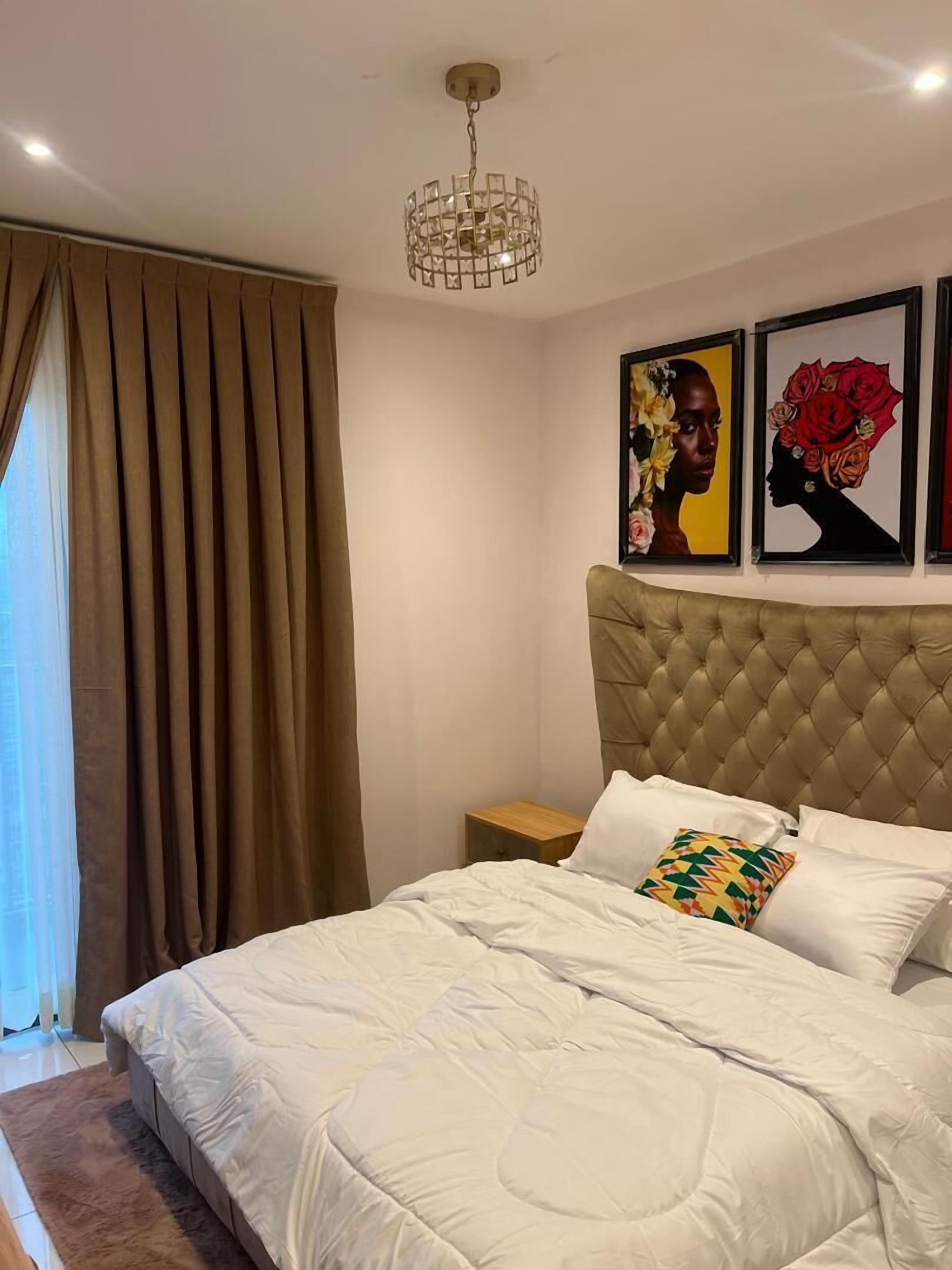 Een slaapkamer met een gestoffeerd hoofdeinde, een groot bed met wit beddengoed, een houten nachtkastje en een hangende lamp.
