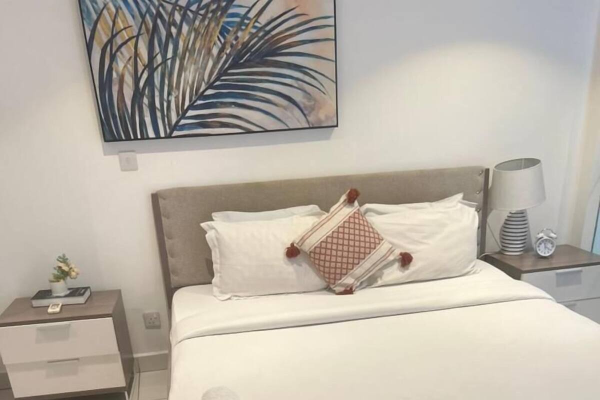 A neatly arranged bedroom with a bed, bedside tables, a red rug, and a wall art piece.